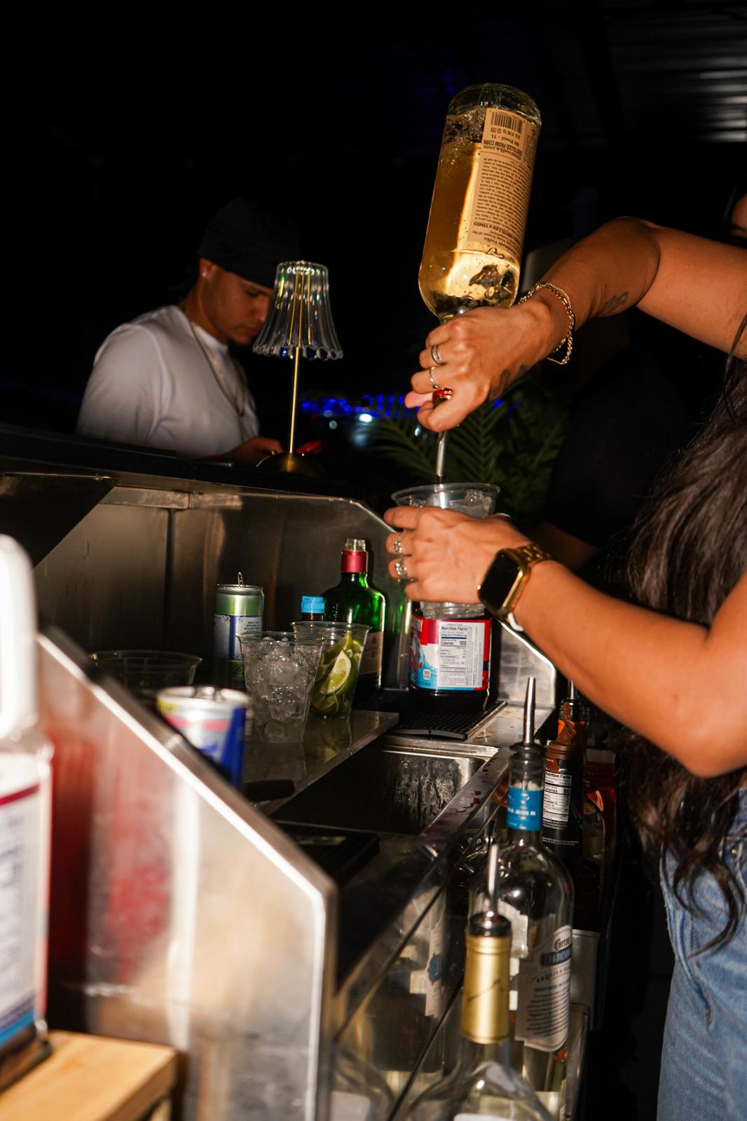 Bartender pouring rum into a cocktail cup at a lively Los Primos night event